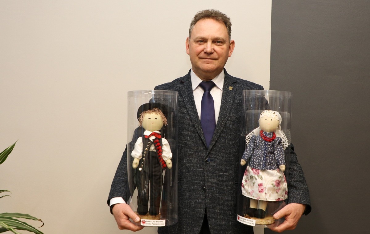 Wicestarosta trzymający w dłoniach dwie lalki do licytacji.