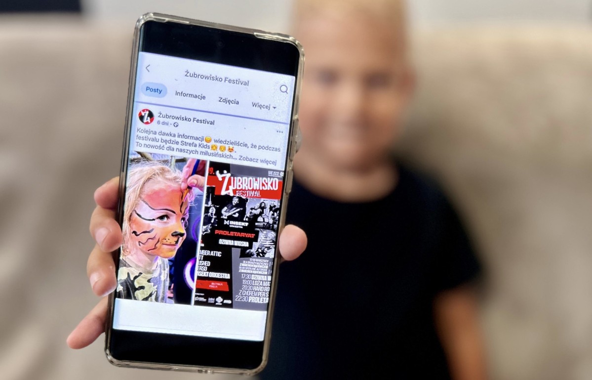 dziecko trzyma w ręku telefon z postem żubrowiska o strefie kids.