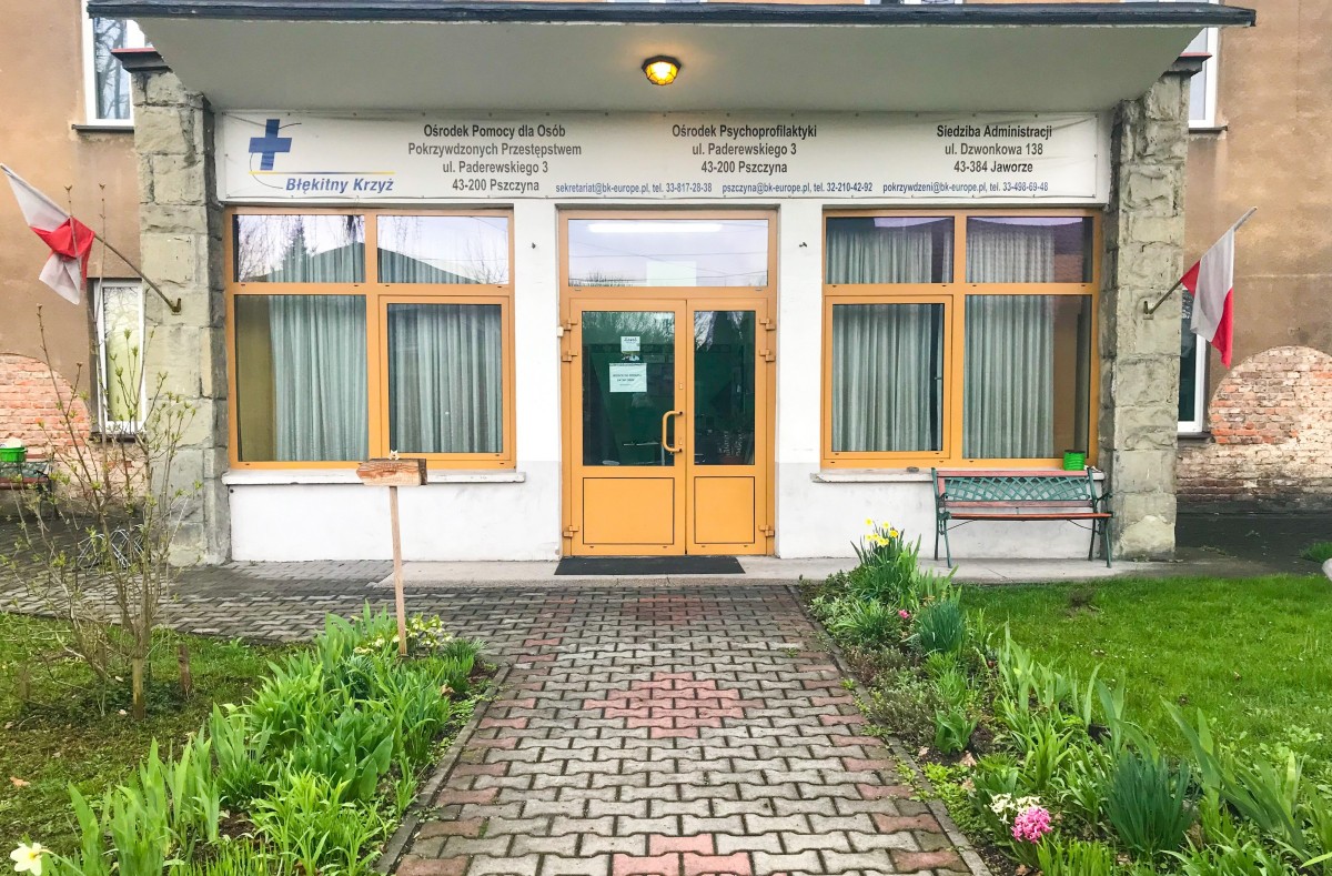 Wejście do budynku, w którym Fundacja Błękitny Krzyż prowadzi poradnię. Stary budynek, dwie flagi Polski.