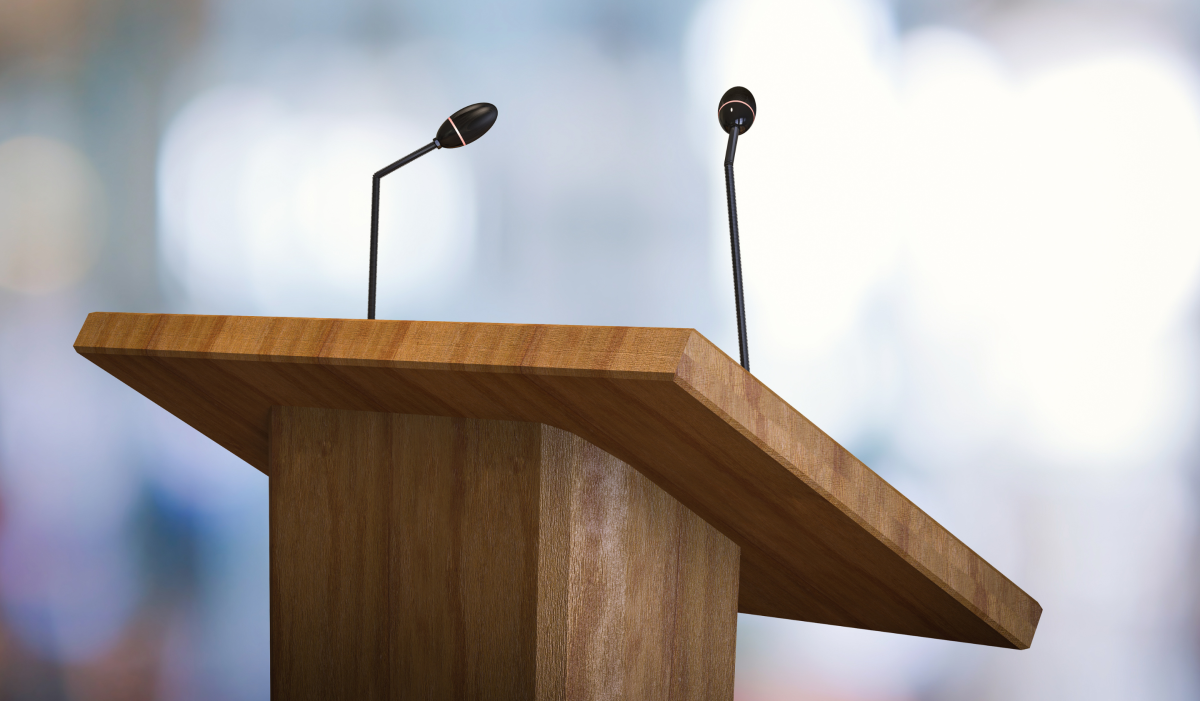 Grafika z mównicą i mikrofonem, informacja z tytułem konferencji, datą i miejscem.