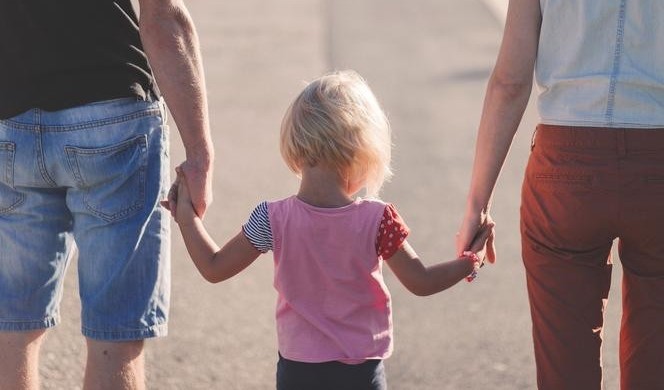 Tata i mama trzymają za ręce dziecko.