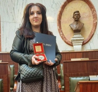 Kobieta stoi w dużej sali, trzymając medal.