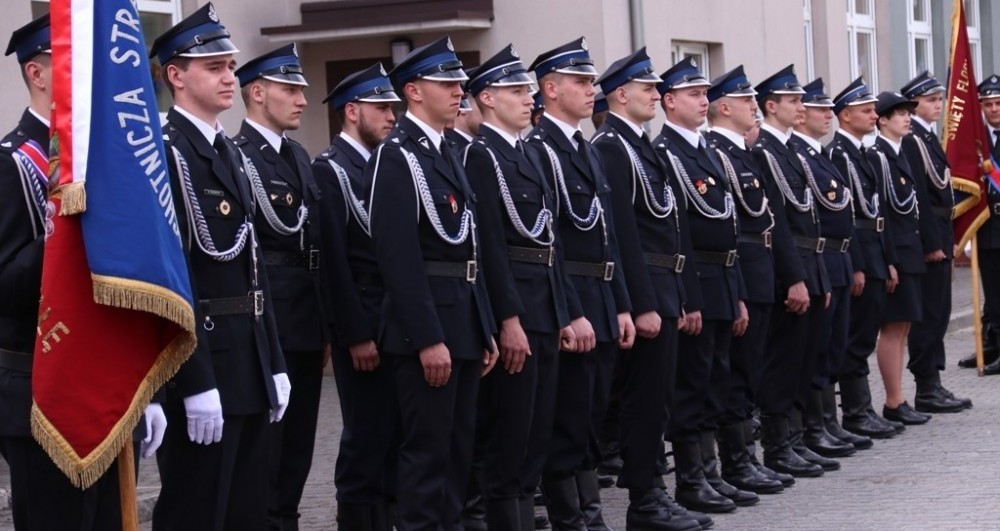 Strażacy w galowych mundurach stojący na baczność w jednym rzędzie.