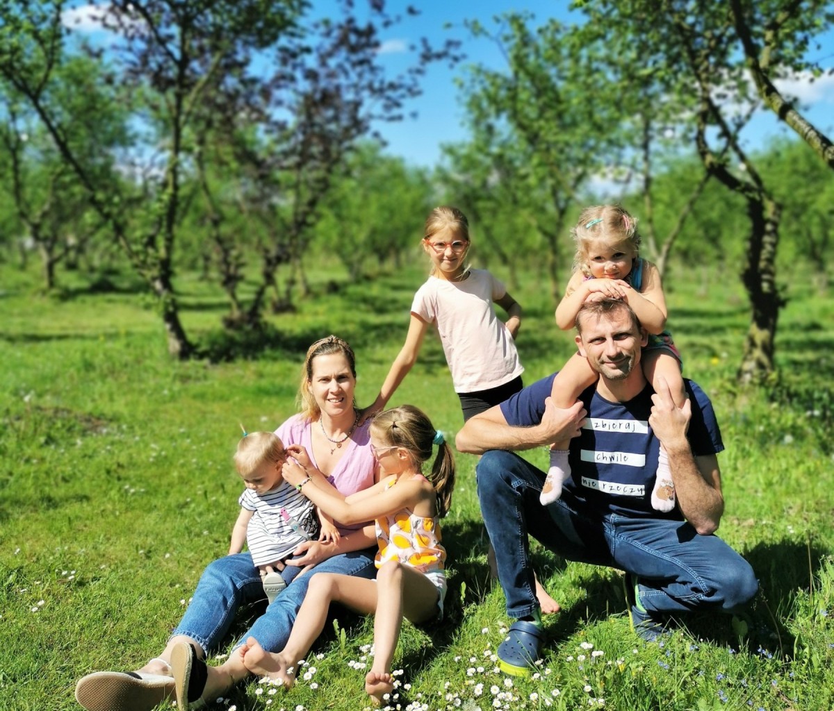 Rodzina - rodzice i 4 dziewczynki siedzą na zielonej trawie na plantacji orzechów laskowych