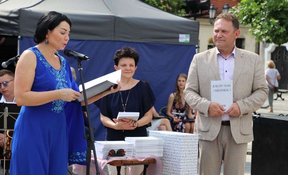 Dyrektor Ogniska Muzycznego w Pszczynie przemawiająca do mikrofonu podczas Koncertu Jubileuszowego i wicestarosta Damian Cieszewski, który w dłoniach trzyma publikację.