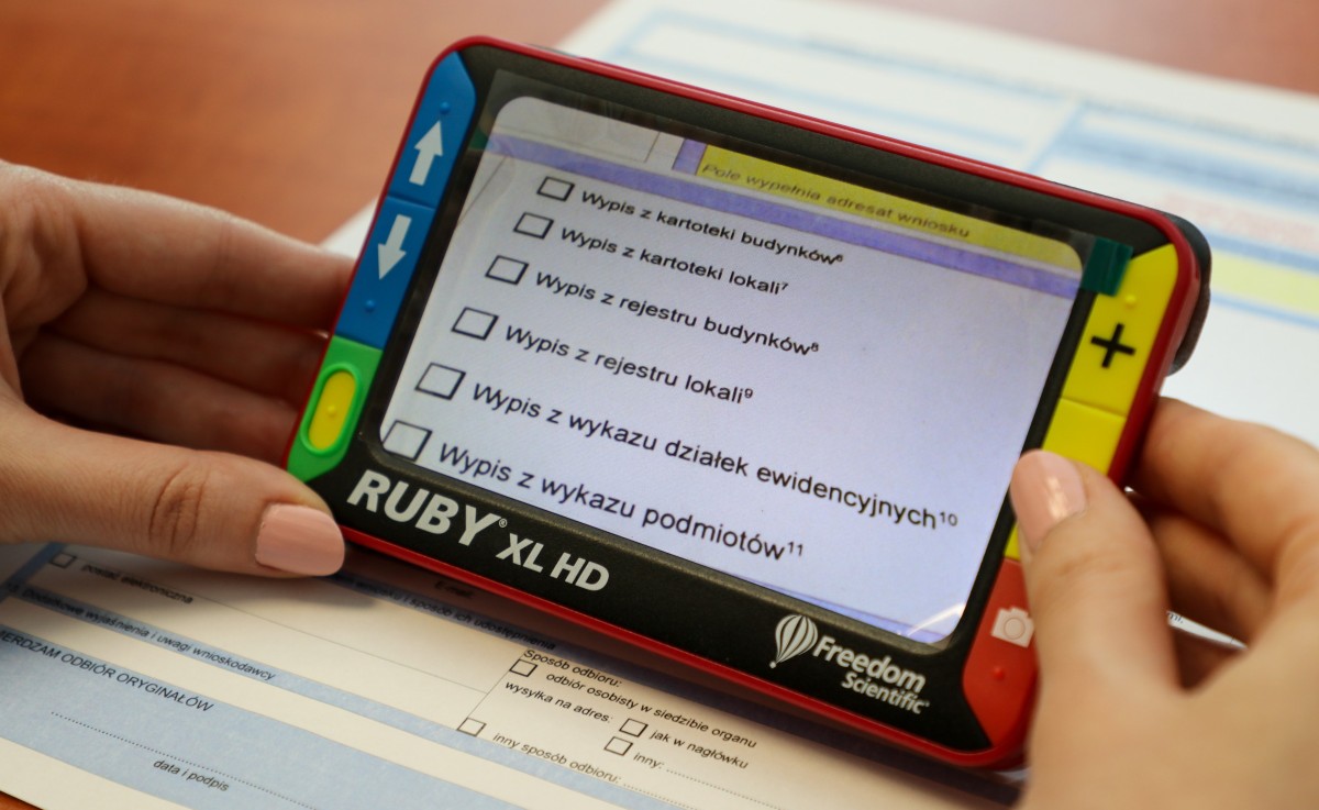 Urządzenie elektroniczne trzymane w dłoniach nad wnioskiem geodezyjnym. Powiększony obraz.
