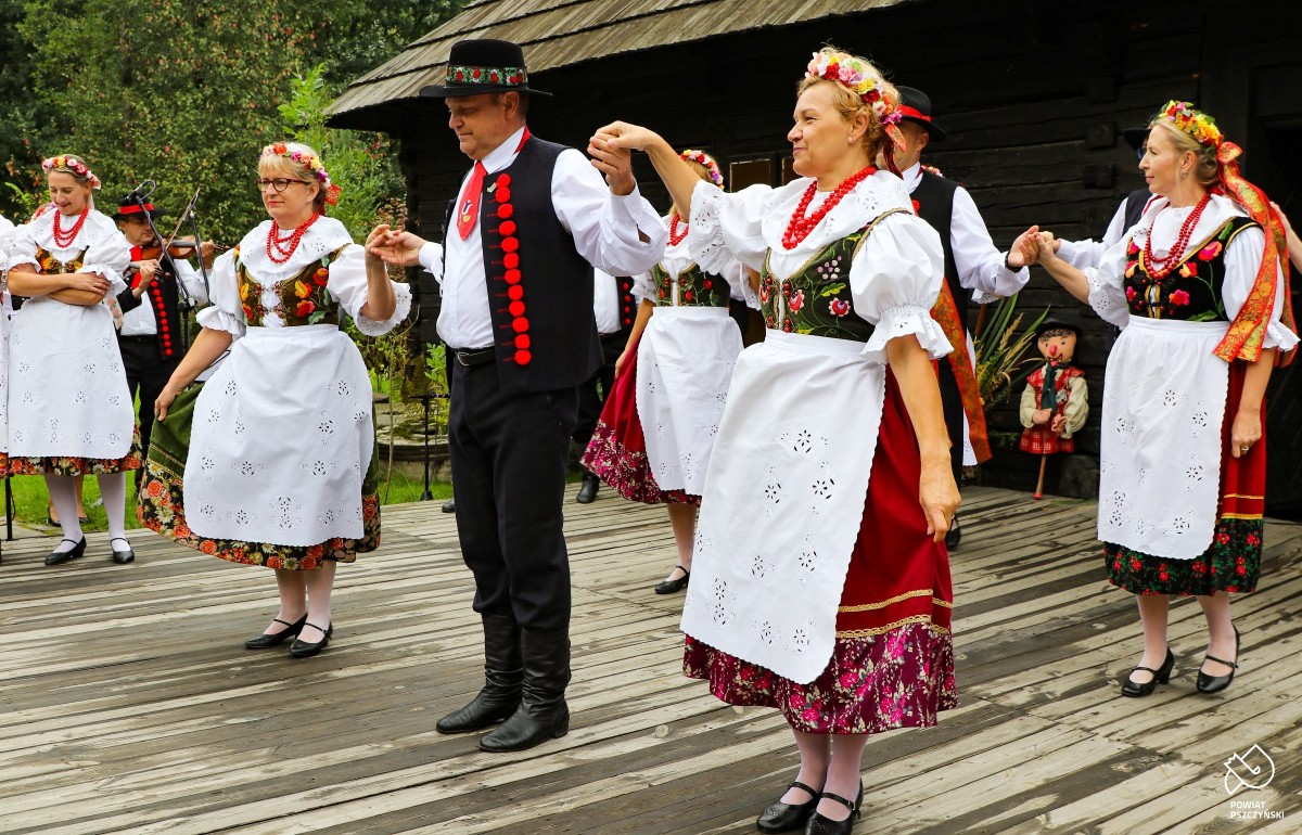 Członkowie Zespołu Regionalnego "Pszczyna" w trakcie występu na scenie przed drewnianą chatą.