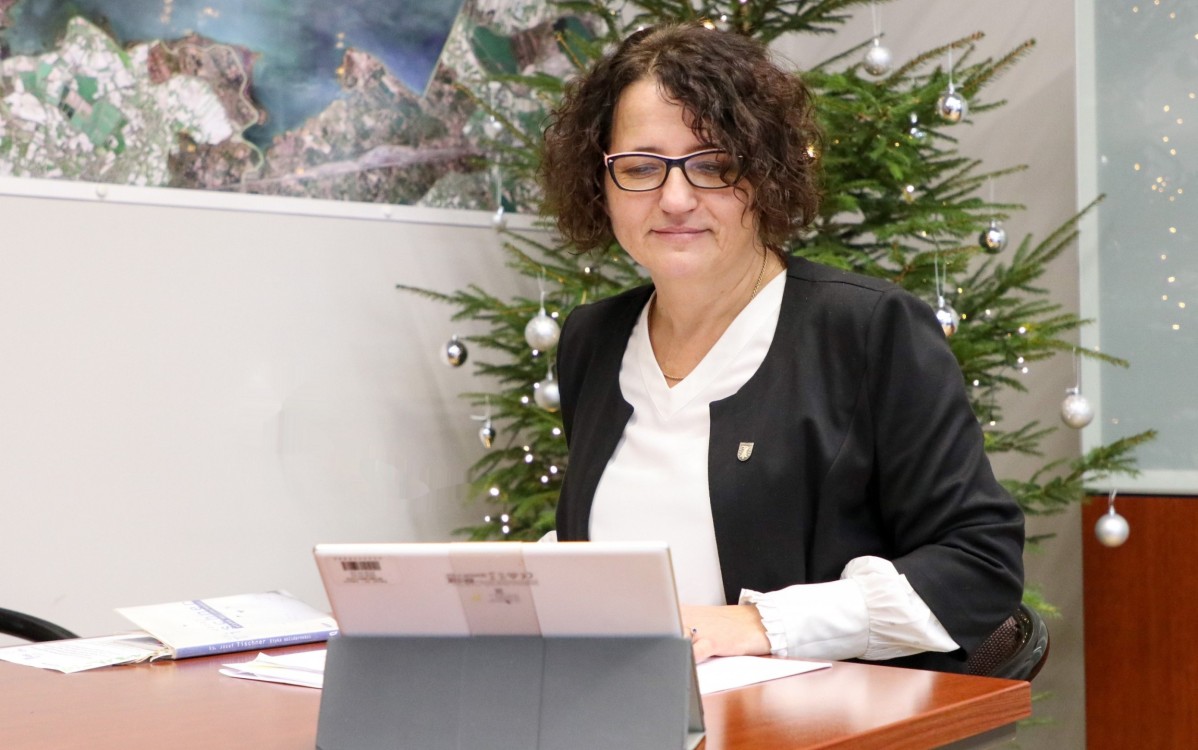 Starosta Barbara Bandoła siedzi za stołem w swoim gabinecie, ma przed soba tablet, trwa sesja rady powiatu online. Za nią stoi choinka.