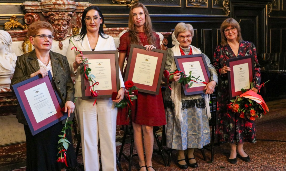 Laureatki odznaczenia stoją w sali lustrzanej zamku, trzymając listy gratulacyjne