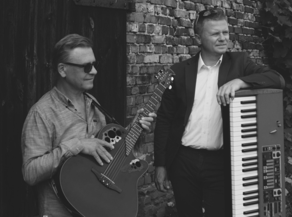 Dwaj mężczyźni, jeden trzyma gitarę, drugi stoi obok klawiszy.