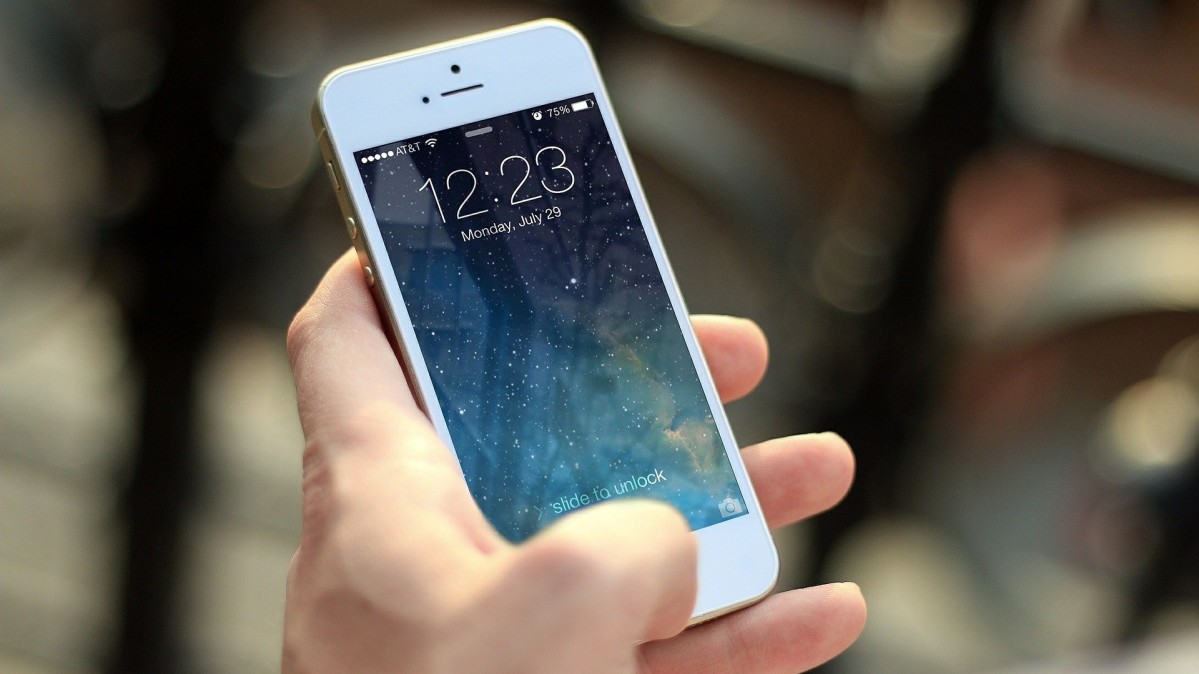 Dłoń trzymająca telefon komórkowy z podświetlonym wyświetlaczem.