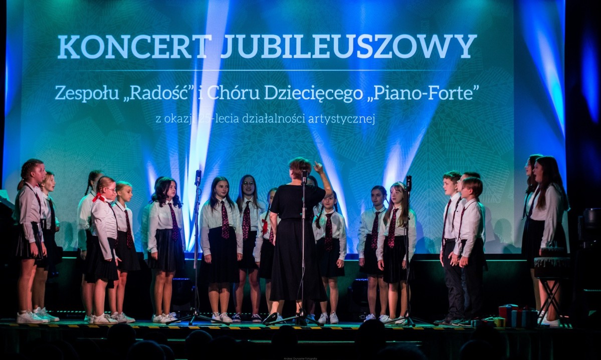 Dzieci w biało-czarnych strojach występują na scenie.