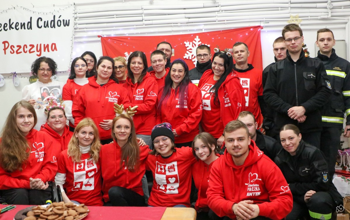 Wolontariusze szlachetnej paczki ubrani w czerwone bluzy, strażacy oraz starosta pozują do wspólnego zdjęcia w magazynie
