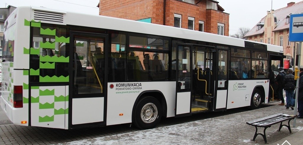 Na przystanku pasażerowie wchodzą do dużego białego autobusu.