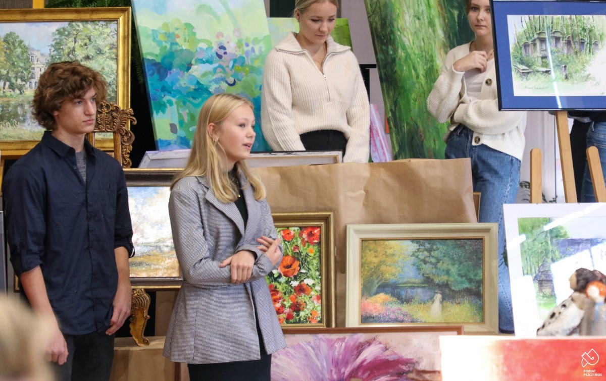 Uczniowie stoją przy obrazach lokalnych artystów