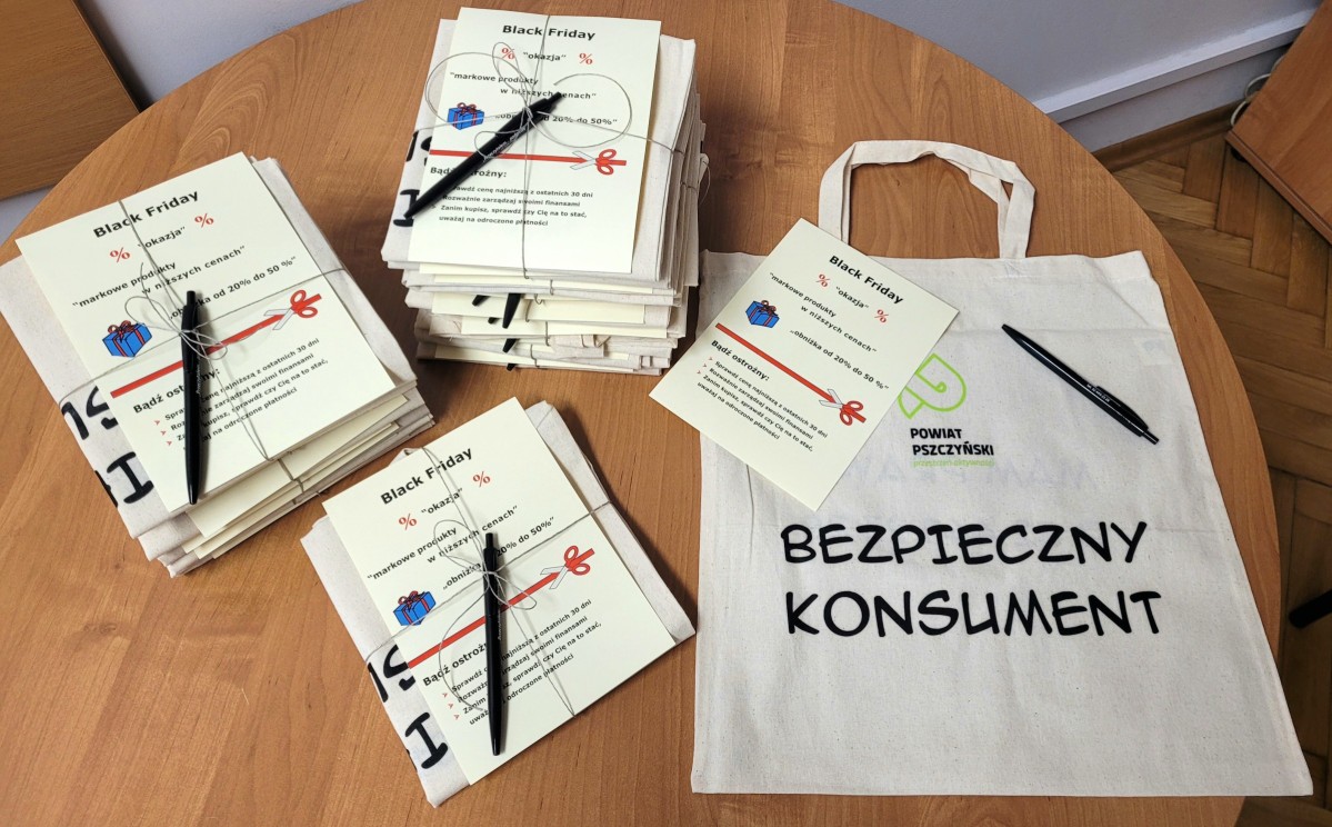 na stole ułżożone ulotki informacyjne dla konsumentów oraz biała torba z naoisem bezpieczny konsument