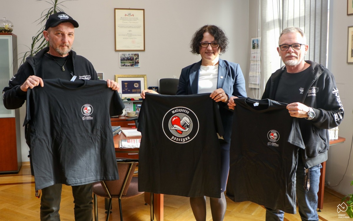 Starosta z przedstawicielami Pszczyńskiej Grupy Motocyklowej w jej gabinecie przed biurkiem trzymają w dłoniach koszulki.