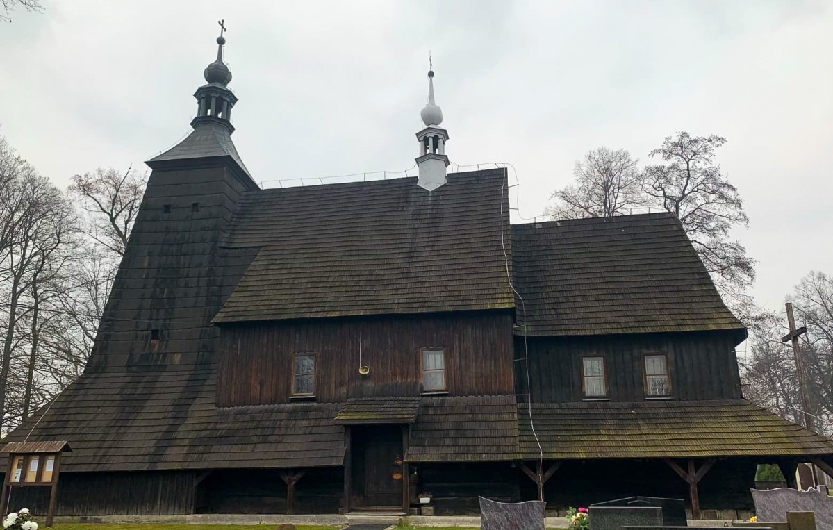 Drewniany zabytkowy kościół w Grzawie po zabiegu fumigacji. Wokół cmentarz.