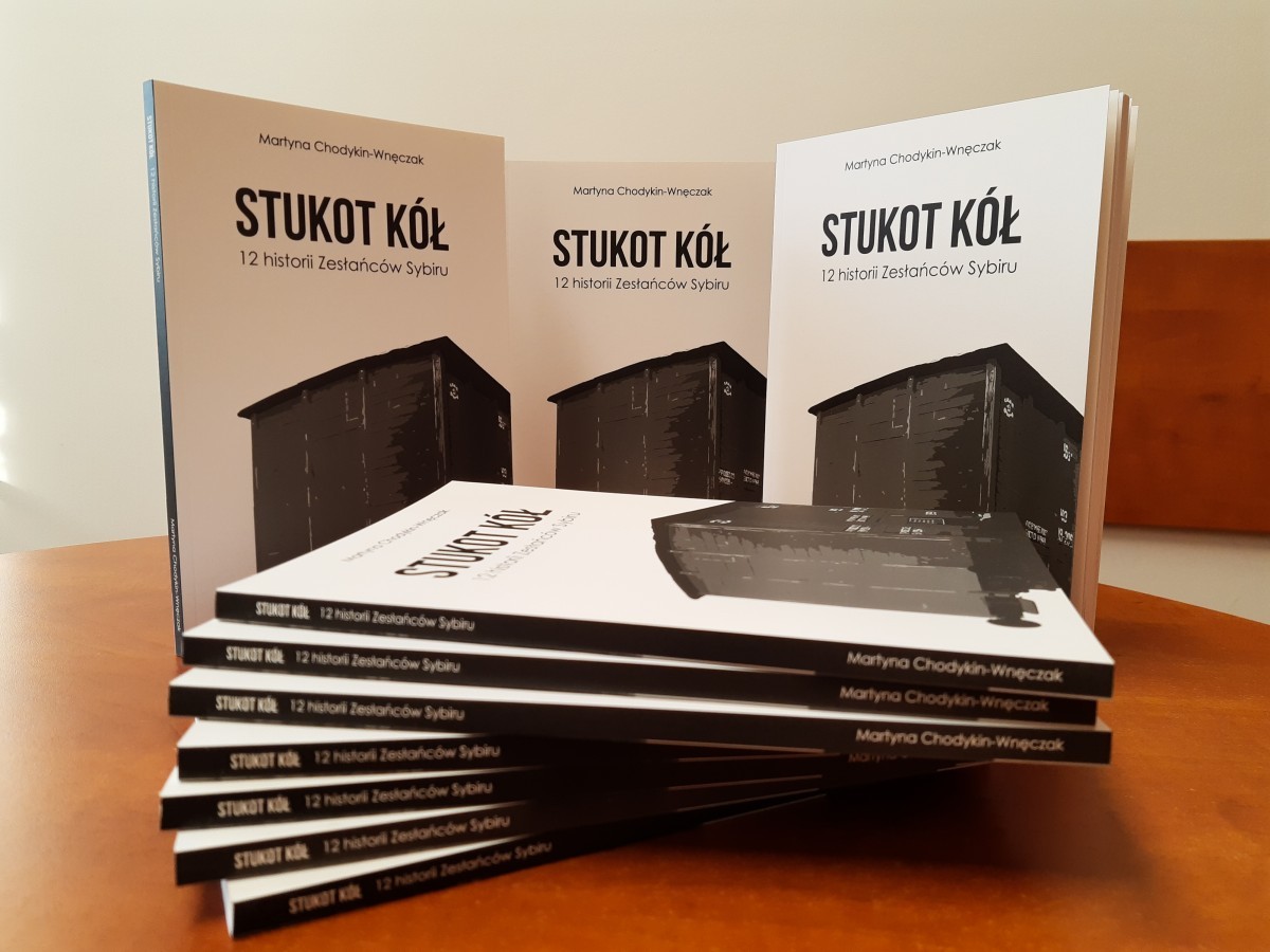 Na stole postawione są trzy książki. Przed nimi położonych jest kilka publikacji.