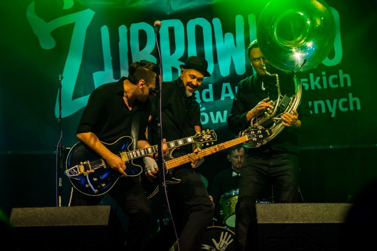 Grafika przedsawiająca trzech muzykow podczas koncertu na scenie doskonale się bawią, spiewają i graja na instrumentach