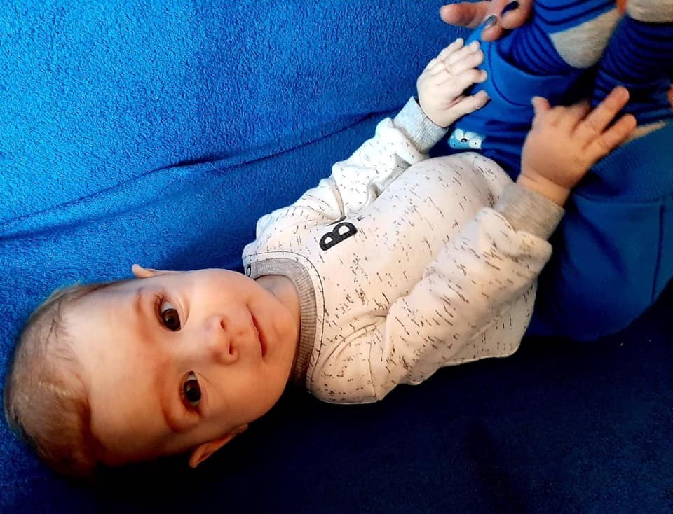 Mały chłopczyk leży na łóżeczku. Uśmiecha się do aparatu