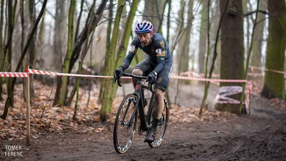 Ubrudzony od błota kolarz w sportowym stroju i kasku na rowerze.