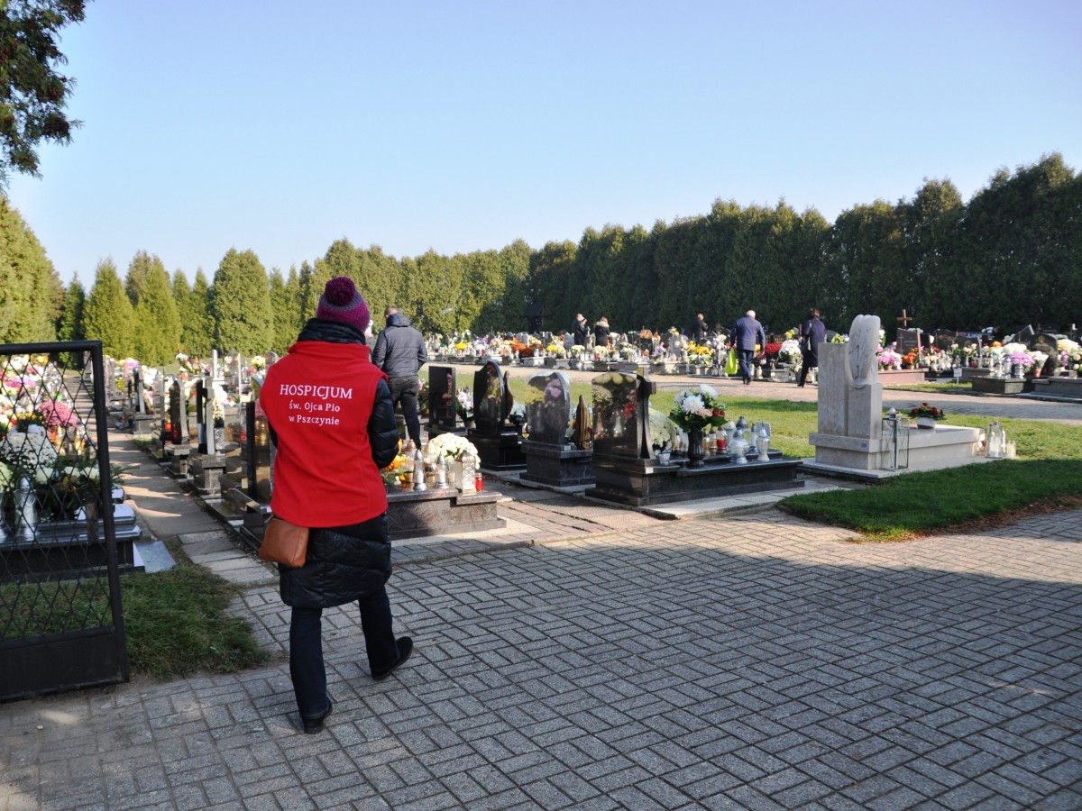 Wolontariusz hospicjum Ojca Pio wchodzi na cmentarz parafialny w Kobielicach. Ma ubrany czerwony polar z nazwą hospicjum.