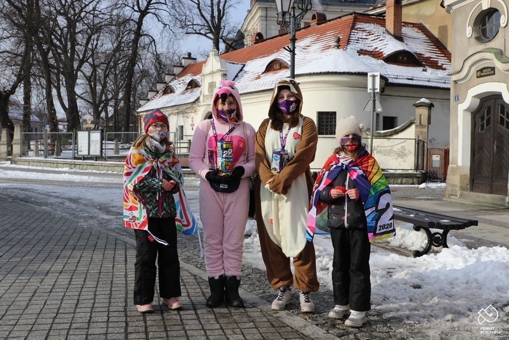 CZTERY MŁODE OSOBY UBRANE W KOLOROWE STROJE NA ZEWNĄTRZ Z PUSZKAMI wIELKIEJ oRKIESTRY śWIĄTECZNEJ pOMOCY
