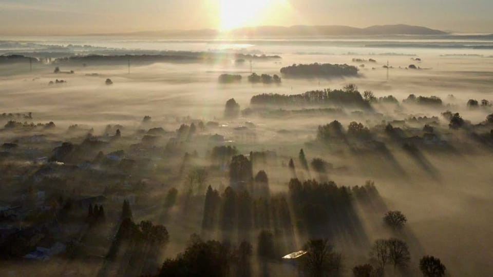 Mgła nad polami wsi. Przed chmury przebija się słońce.