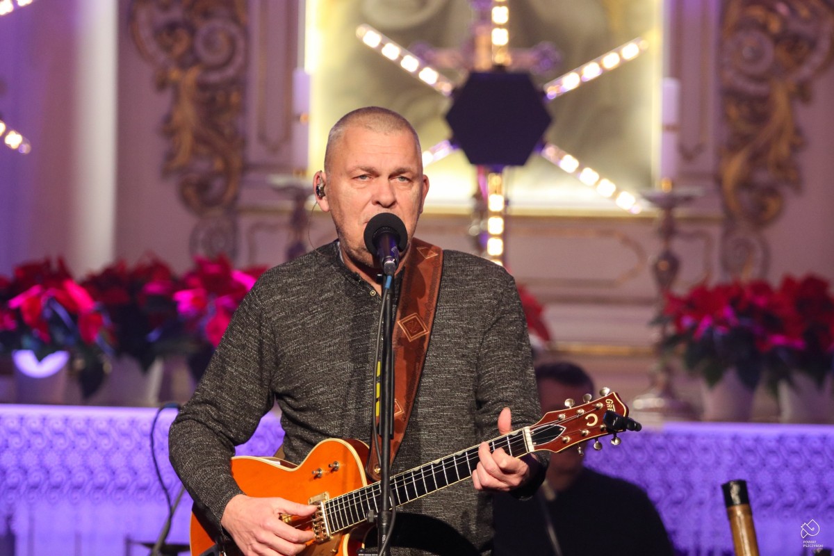Adam Nowak, wokalista zespołu Raz Dwa Trzy w kościele ewangelickim śpiewa piosenkę do mikrofonu, grając na gitarze