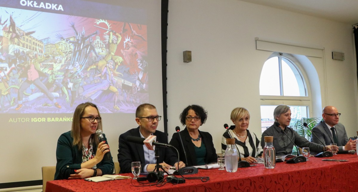 W sali stajni książęcych za stołem siedza osoby biorące udział w konferencji prasowej.